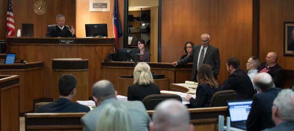 A lawyer stands in front of a judge and jury in a courtroom, representing a client in a criminal case.