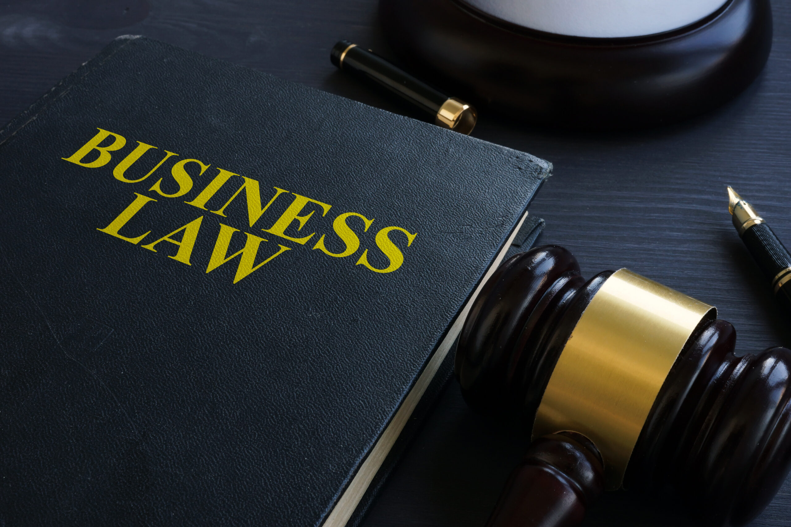 A gavel resting on a closed book titled 'Business Law' with two fountain pens on the side.