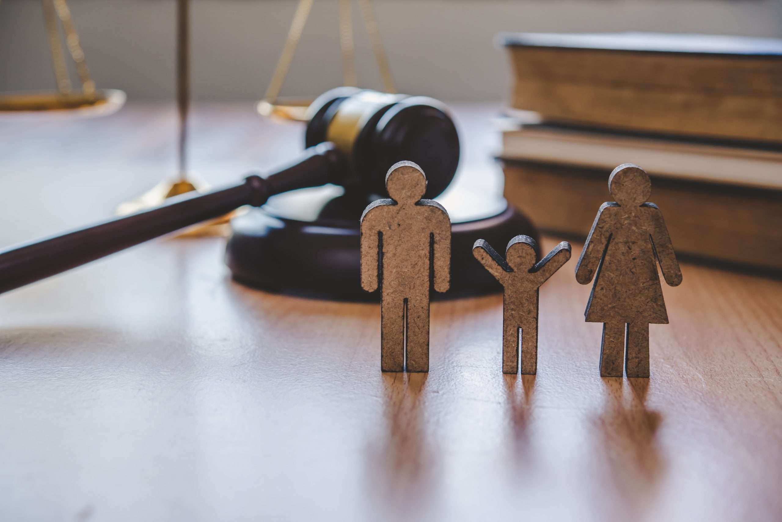 A gavel and books sit on a wooden table with wooden figures of a family in front of it.