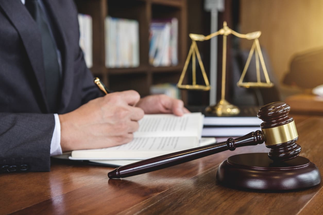 A personal injury lawyer is writing in a notebook while sitting at his desk with a gavel and scales of justice in the foreground.