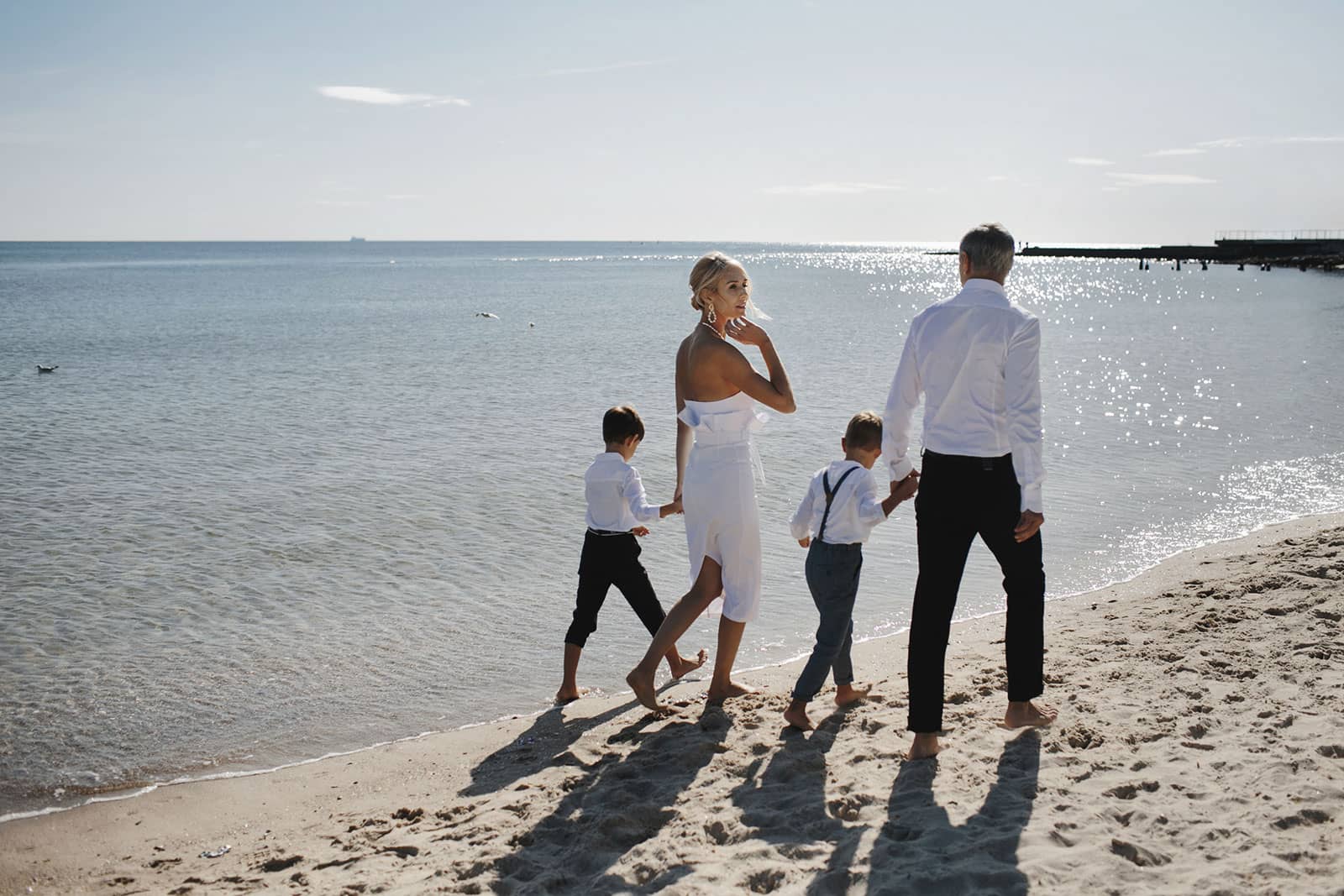 Family holding hands and walking on the beach in formal clothing.