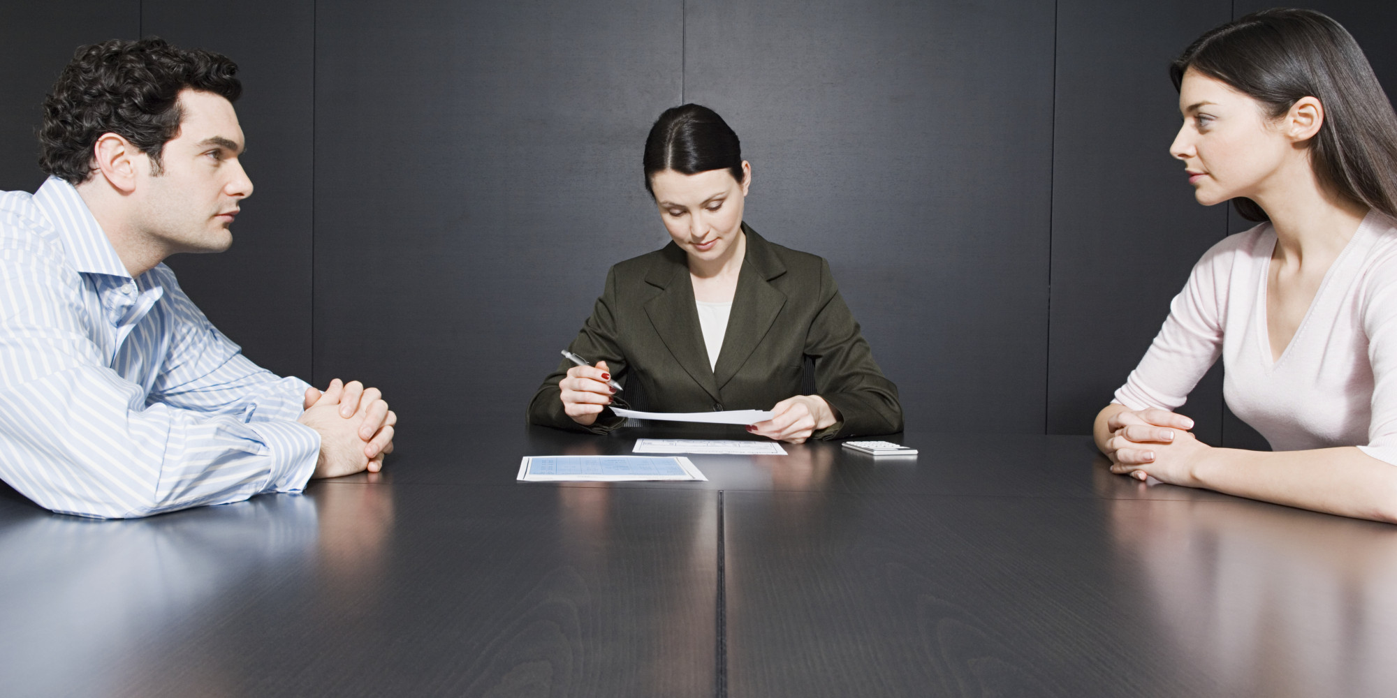 A divorce attorney sits at a conference table with her clients, a man and a woman, and reviews a document.