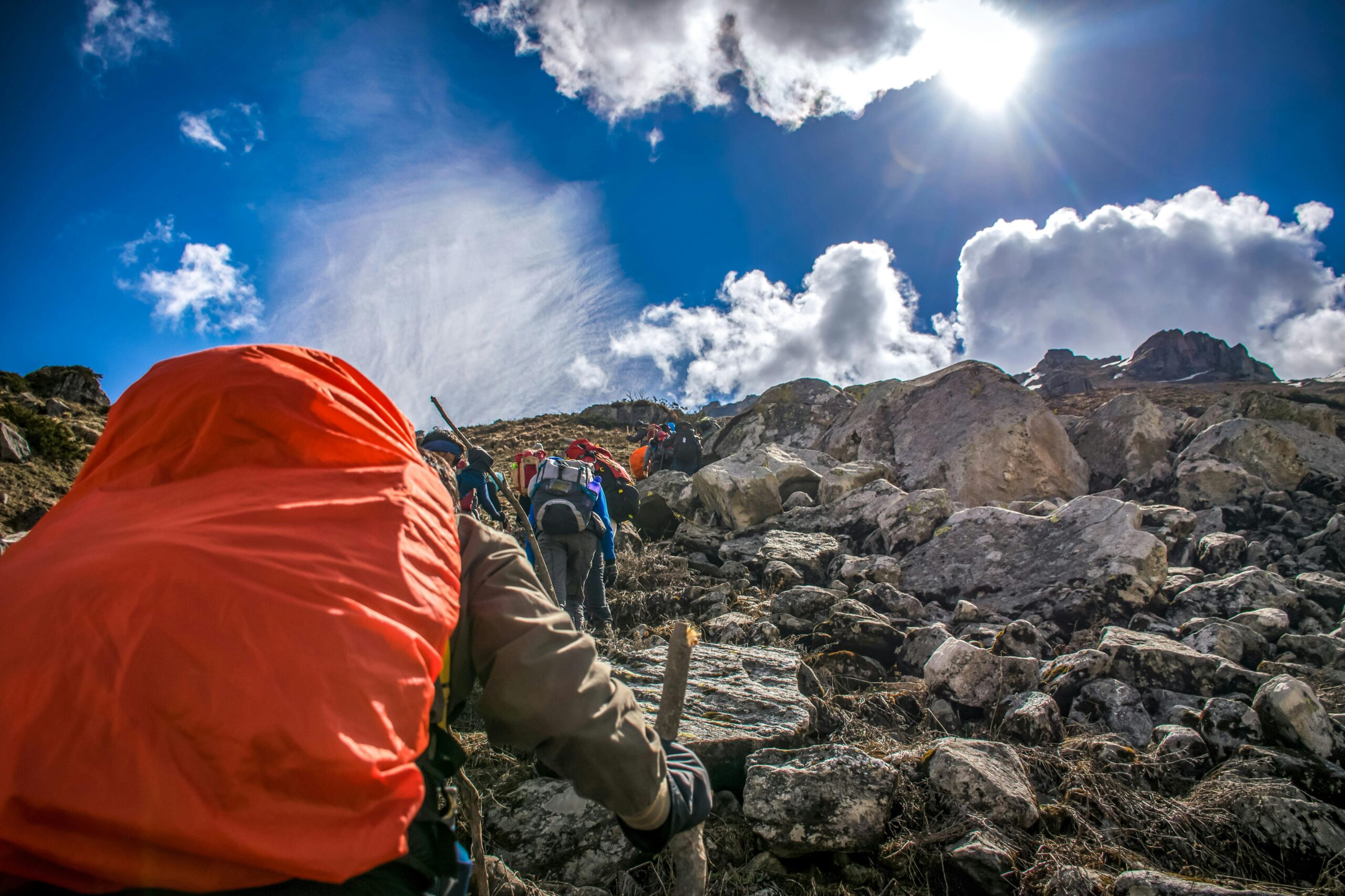 A group of hikers ascend a steep rocky slope in the Andes Mountains under a bright blue sky.