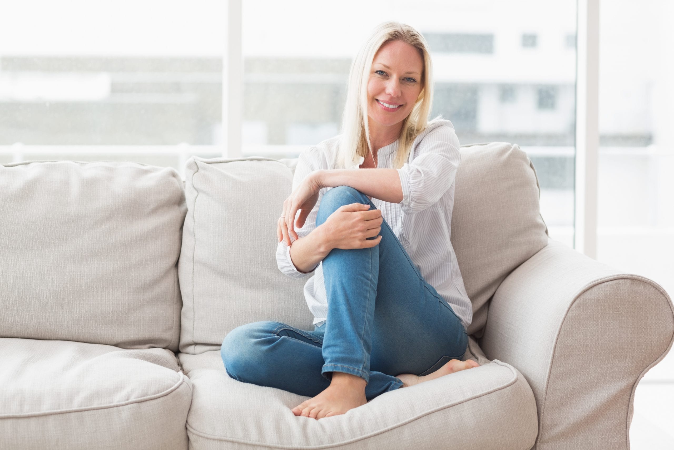 A blonde woman in jeans and a white shirt is sitting on a couch with her legs curled up and smiling at the camera while sitting in front of a laptop with a headline reading '6 tips for creating captivating content'.